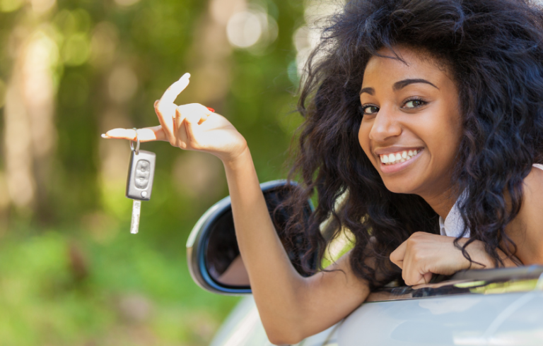 teenage girl siting in driver's seat leaning out window holding car keys